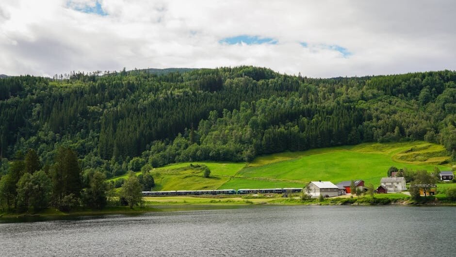 A picturesque view of a train traveling through Norway's lush green countryside near a tranquil lake.