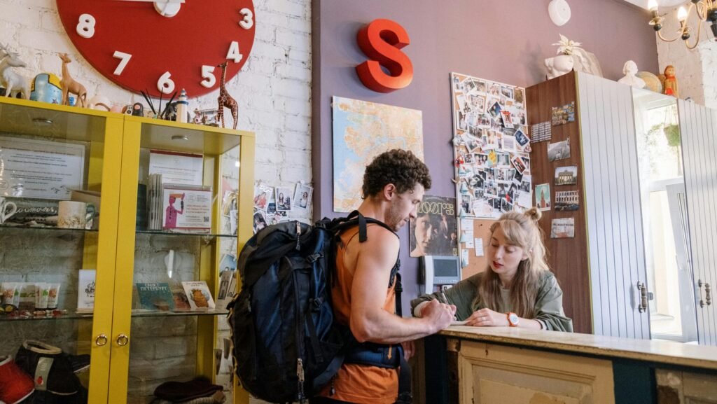 A backpacker at a hostel front desk getting assistance from a receptionist.