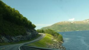 Breathtaking view of a winding road along a Norwegian fjord, surrounded by water and lush greenery.