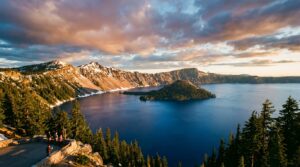 Panoramic view of Crater Lake's deep blue water and Wizard Island from Rim Village overlook at sunset