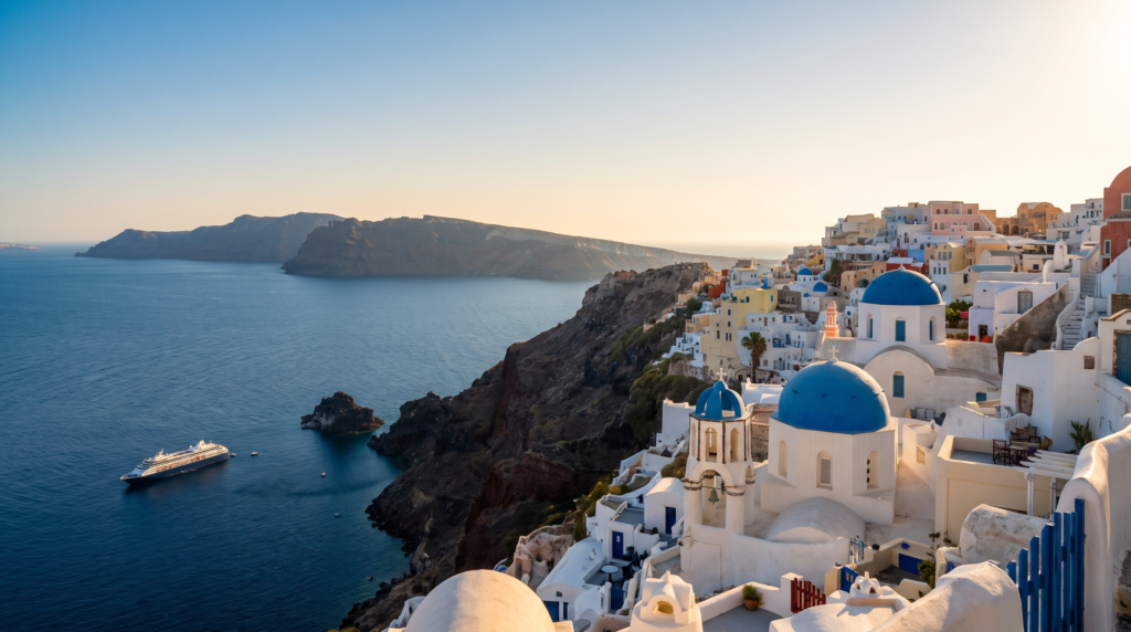 Whitewashed houses and blue-domed churches on the Santorini caldera cliffs above the Aegean Sea at golden hour