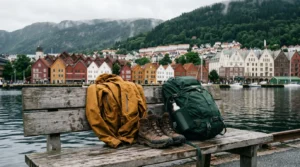 Rain jacket, hiking boots and a daypack on a wooden bench in front of Bergen's colourful Bryggen wharf and fjord, Norway